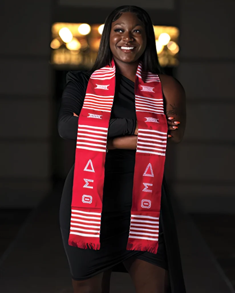 Smiling graduate wearing a red Delta Sigma Theta stole and black attire.