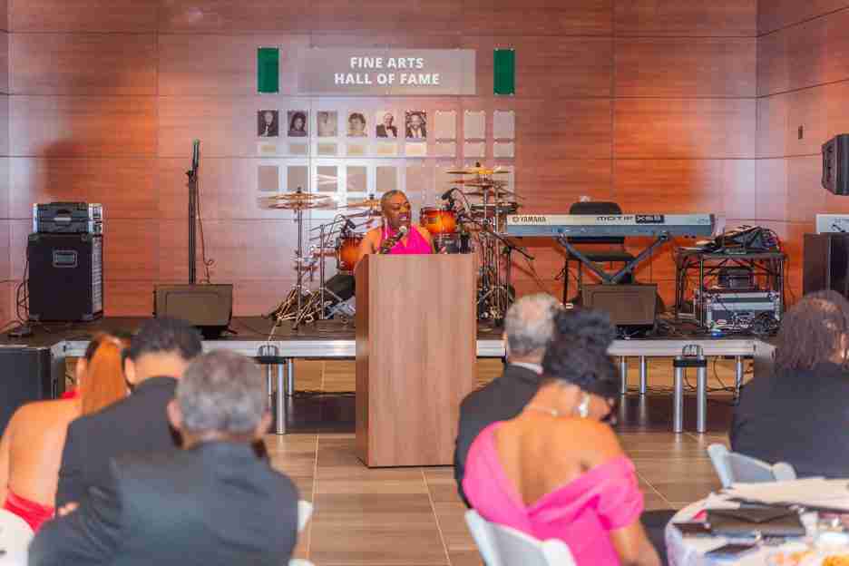 Speaker addressing an audience in a hall with musical instruments on stage.