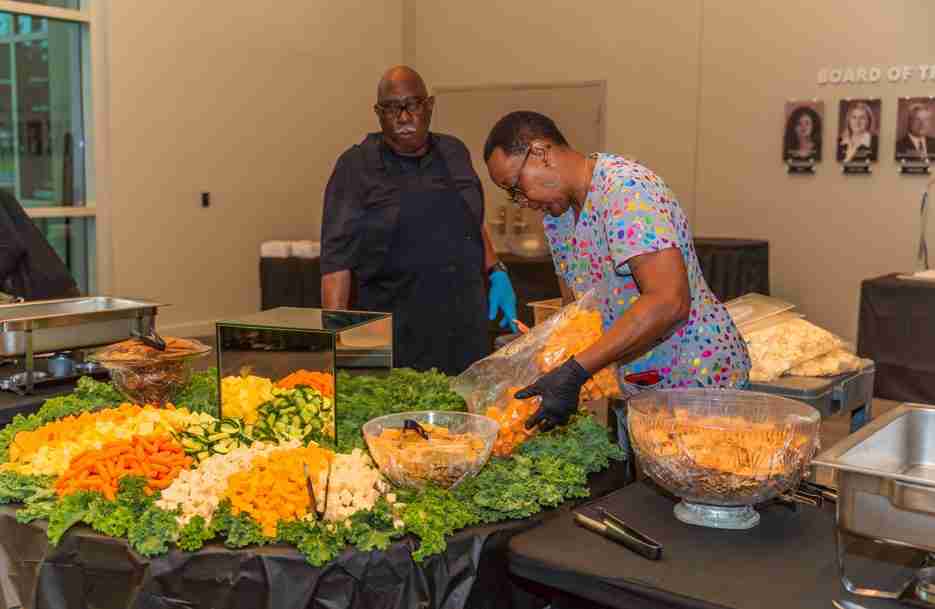 Two women preparing food at a buffet table with various dishes.
