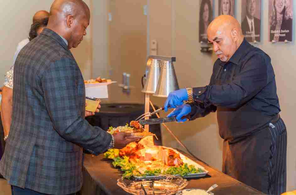 A man serving carved roasted meat to a guest at a buffet.