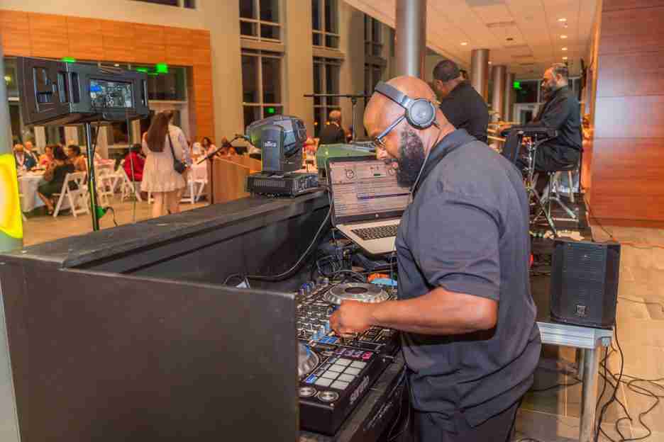 A DJ wearing headphones mixes music at a lively indoor event.