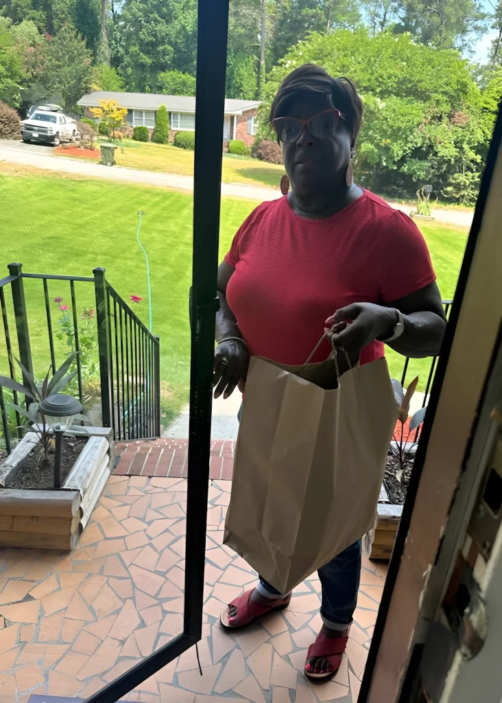 A woman in a pink shirt holding a paper bag at a doorway.