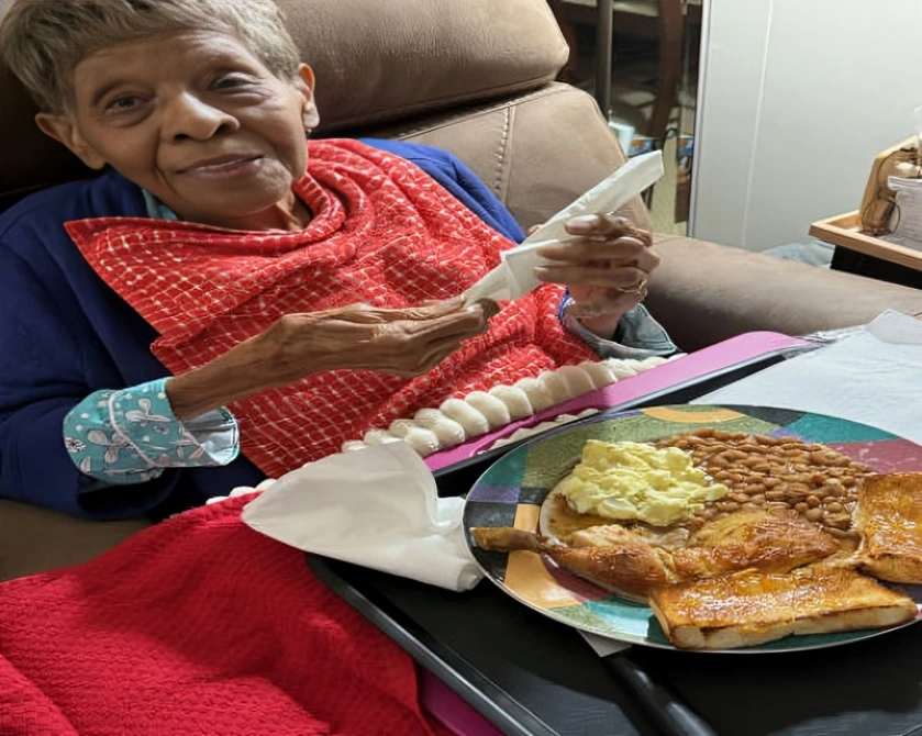 Elderly woman enjoying a meal with bread and a drink.