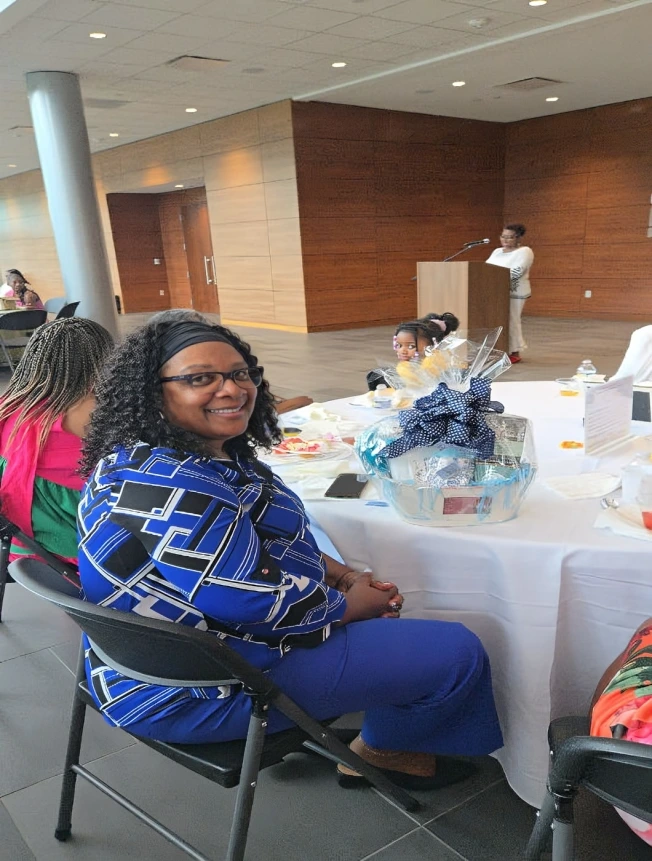 Woman smiling at a formal event, seated at a table with gift baskets.