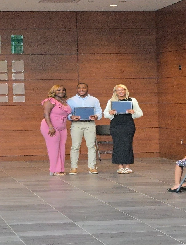 Three individuals on a stage holding certificates.