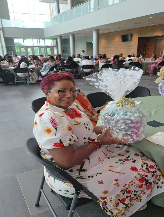 Woman in floral dress holding a gift basket at a social gathering.