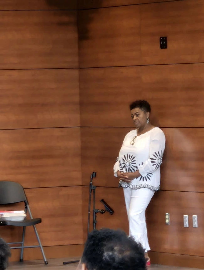 A man in a white outfit speaking with a microphone in a wooden room.