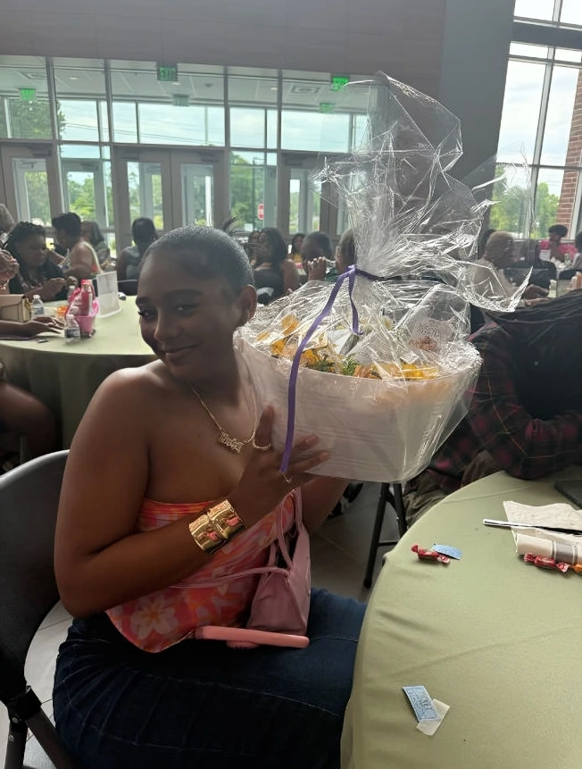 Woman in a pink dress holding a gift basket wrapped in cellophane at a restaurant.