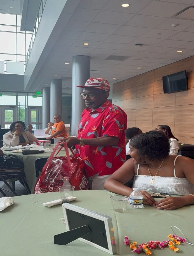 Man in red shirt and cap standing in a café or restaurant.