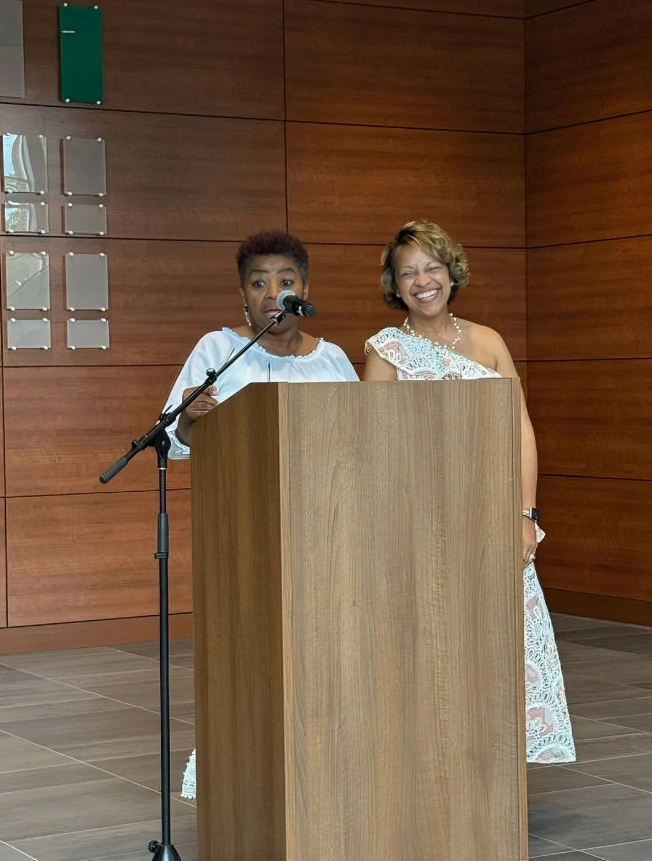 Two people speaking at podiums in a wooden-paneled room.