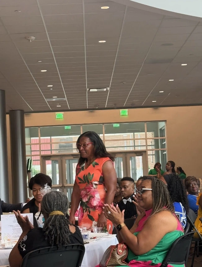 Woman in an orange dress walking through a crowded room with seated people.