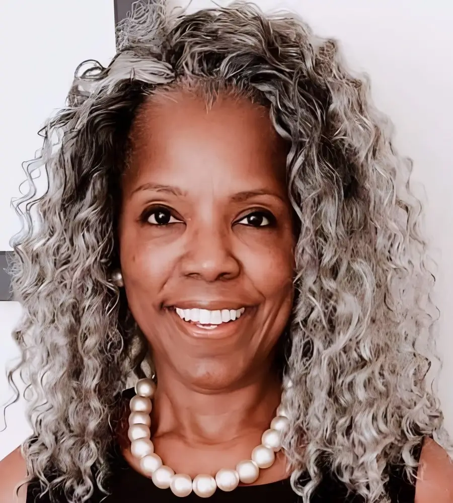 Smiling woman with gray curly hair and pearl necklace.