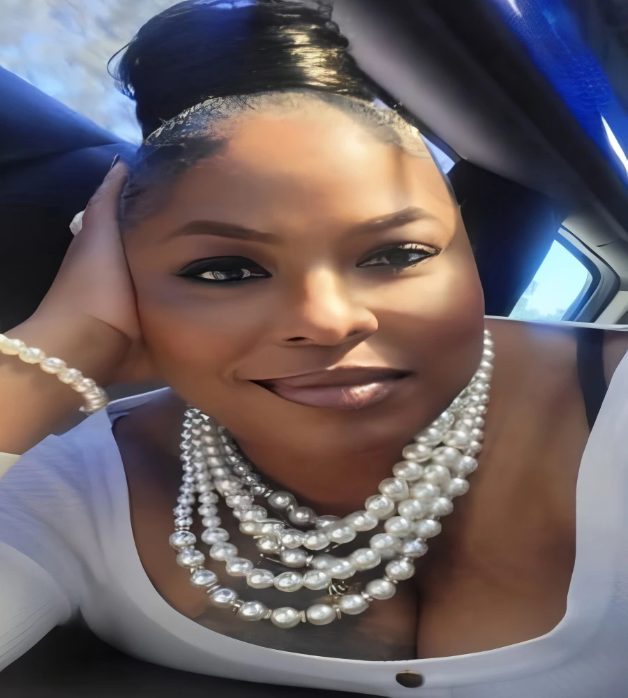 Confident woman wearing layered pearl necklaces and a white top, smiling in a car.